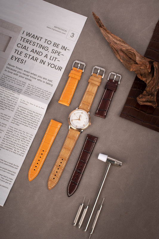Handcrafted Mississippi alligator leather straps with quick-release system, compatible with Omega Seamaster, Rolex Datejust & IWC Pilot. 12 curated colors (caramel/amber/orion black), 3.5mm French edge stitching, 2.0mm spring bars. Each scale pattern hand-aligned, customizable length/stitch color/hardware engraving.